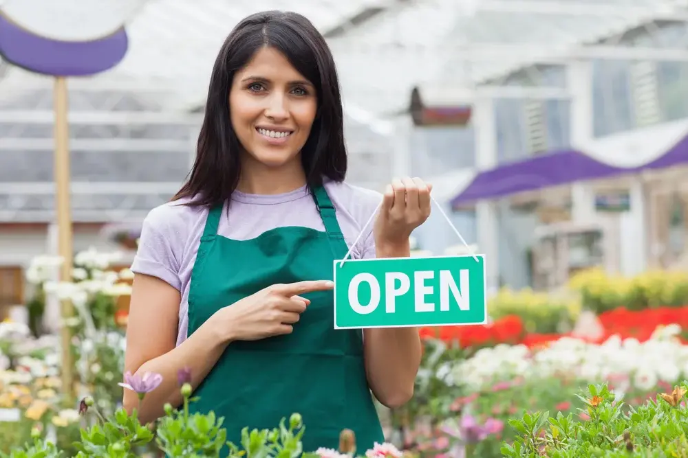 Woman in garden center pointing at the open-sign while smiling